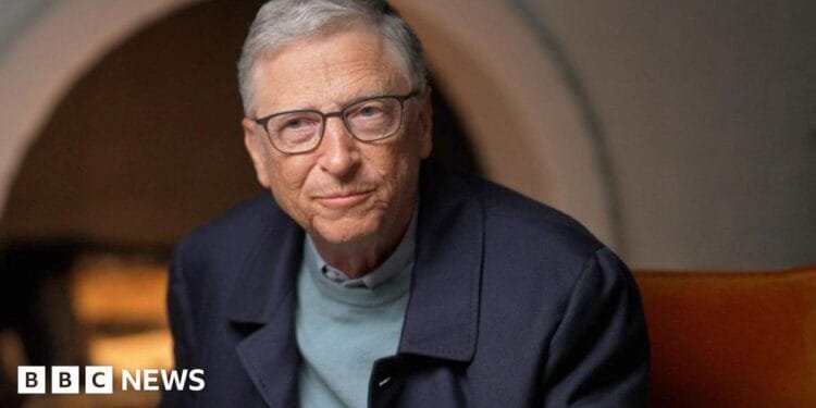 Bill Gates in blue jumper and jacket, sitting by fireplace