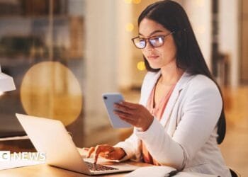 A woman sitting at her computer and using her phone