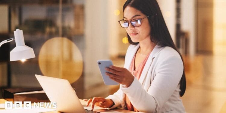 A woman sitting at her computer and using her phone