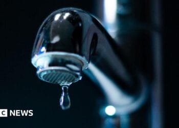Keir Starmer, in a white lab coat, points at a computer screen, watched by a young man and women in lab coats and safety goggles. He is on a visit to the Manufacturing Futures Lab at University College London