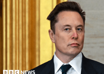 Elon Musk wearing a sharp black suit and tie